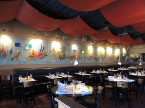 Interior of a restaurant featuring colorful wall art, orange drapery, and neatly set tables.