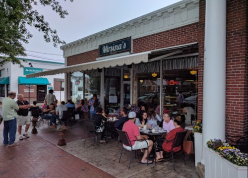 A bustling café with outdoor seating, patrons enjoying meals, and a welcoming storefront on a sunny day.