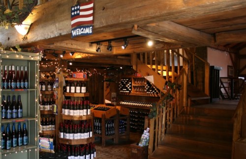 Interior of a rustic wine shop with wooden beams, shelves of wine bottles, and a welcoming sign.