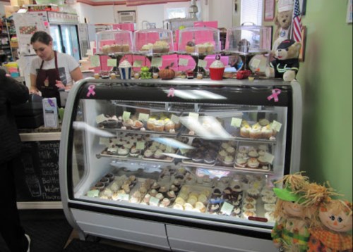 A display case filled with various cupcakes, with a staff member serving in a cozy bakery setting.