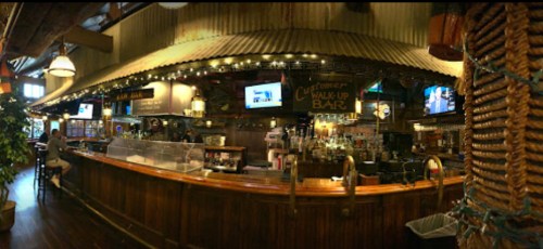 A rustic bar interior with wooden decor, multiple screens, and patrons enjoying drinks in a cozy atmosphere.
