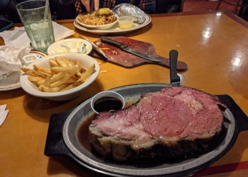 A large serving of prime rib with a side of fries and dipping sauce on a table, with another plate in the background.