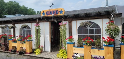 A charming café with colorful flower boxes and hanging plants, featuring a sign that reads "CAFE" above the entrance.
