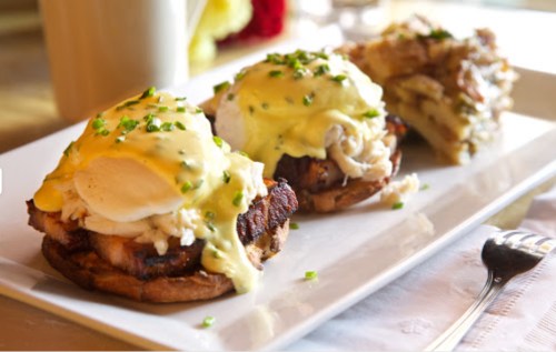 Three eggs Benedict on toasted English muffins, topped with hollandaise sauce and garnished with chopped chives.
