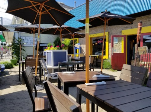 Outdoor dining area with wooden tables, umbrellas, and vibrant plants in a sunny setting.