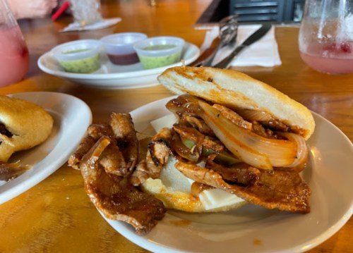 A sandwich filled with grilled chicken, onions, and sauce, served with crispy pork strips on a plate.