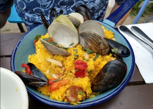 A colorful plate of seafood paella with clams, mussels, peppers, and herbs on a blue dish.