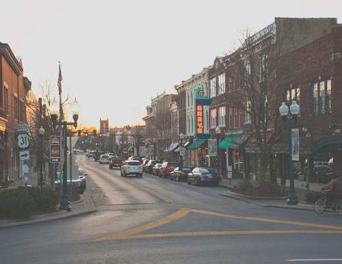 A quaint downtown street at sunset, lined with shops and parked cars, creating a warm, inviting atmosphere.