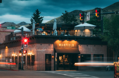 A restaurant with outdoor seating at dusk, located at a street corner with traffic lights and mountains in the background.