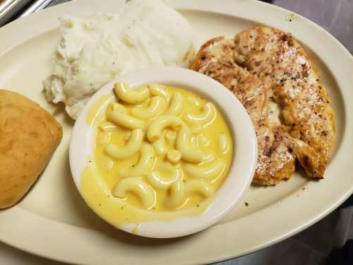 A plate with mashed potatoes, grilled chicken, macaroni and cheese, and a roll.