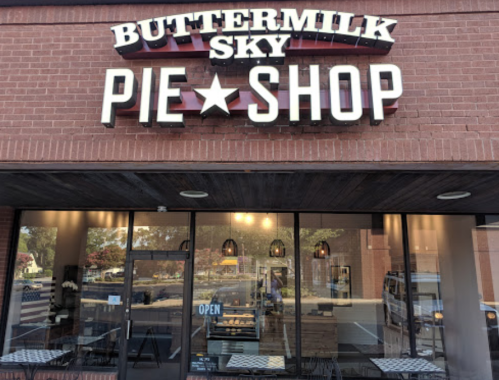 Exterior of Buttermilk Sky Pie Shop, featuring a sign and large windows with tables inside. Open sign visible.