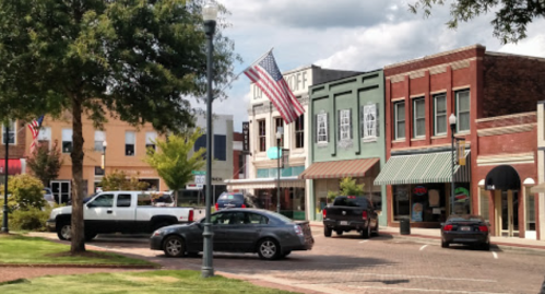 A small town street with shops, parked cars, and an American flag waving in front of a building.