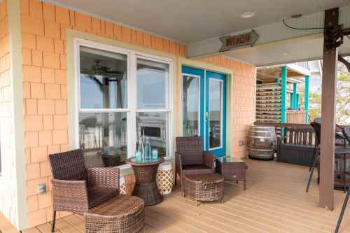 A cozy porch with wicker chairs and a table, featuring orange siding and blue accents, overlooking a scenic view.
