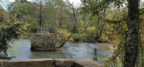A serene river scene with trees and a stone structure in the water, surrounded by autumn foliage.