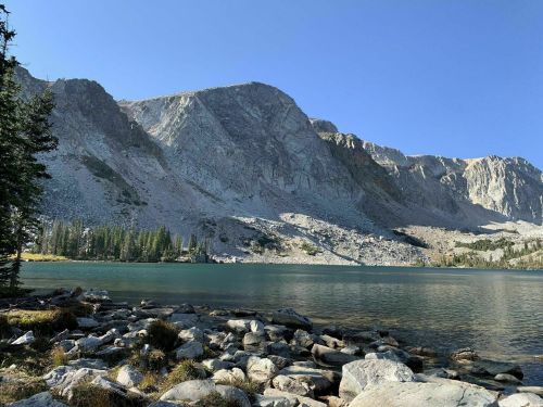 A serene lake surrounded by rocky shores and towering mountains under a clear blue sky.