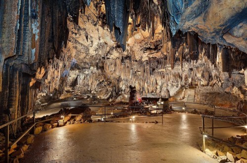 A vast cave interior with stalactites and stalagmites, illuminated pathways, and rocky formations.