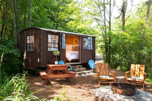 A cozy cabin in a wooded area, featuring a picnic table, two chairs, and a fire pit outside.