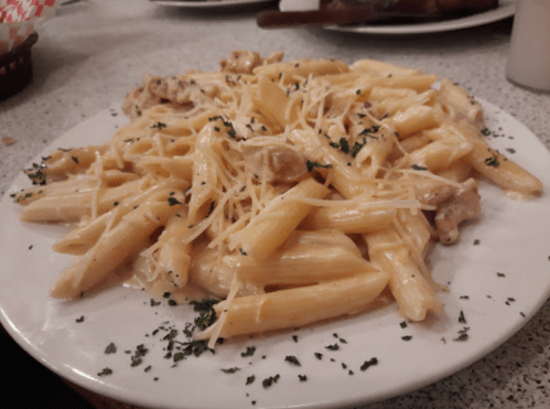 A plate of creamy penne pasta topped with grated cheese and herbs, served on a white dish.