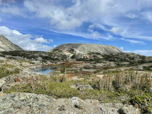 A scenic landscape featuring a calm lake surrounded by rocky terrain and mountains under a partly cloudy sky.