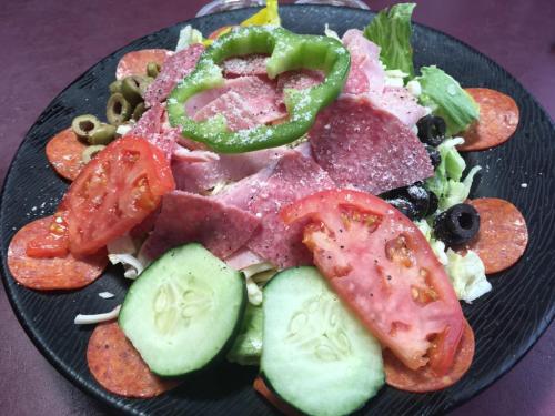 A colorful salad with lettuce, tomatoes, cucumbers, green peppers, olives, and slices of salami and pepperoni on a black plate.