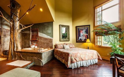 Cozy bedroom with a large bed, a jacuzzi, and a tree feature, surrounded by warm colors and natural light.