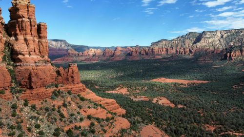 A panoramic view of red rock formations and green vegetation under a blue sky in a desert landscape.
