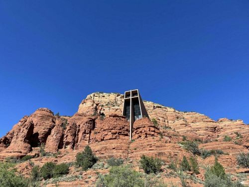 A modern building perched on a red rock formation under a clear blue sky.