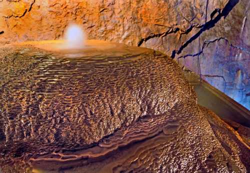 A close-up of a textured rock formation with a small water feature, illuminated by warm, colorful lighting.