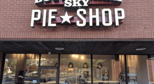 Exterior of a pie shop with a sign that reads "Big Sky Pie Shop" and large windows showcasing the interior.