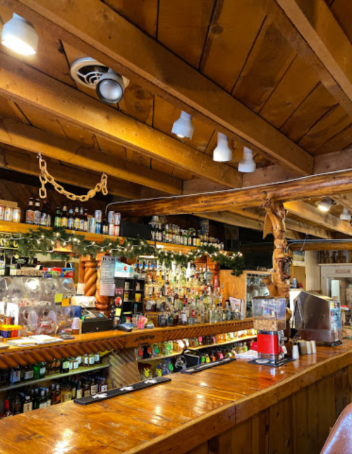 A rustic bar with wooden beams, shelves filled with bottles, and festive decorations in a cozy setting.