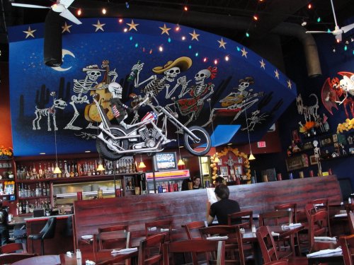 A vibrant restaurant interior featuring a motorcycle suspended from a colorful mural of skeletons playing music.