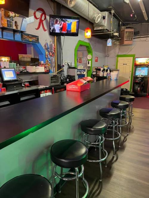A bar with a sleek black countertop, several stools, and a TV displaying colorful images in a vibrant setting.