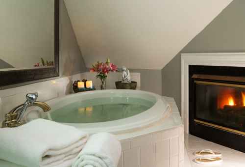A cozy bathroom featuring a round bathtub, candles, flowers, and a fireplace, creating a relaxing atmosphere.