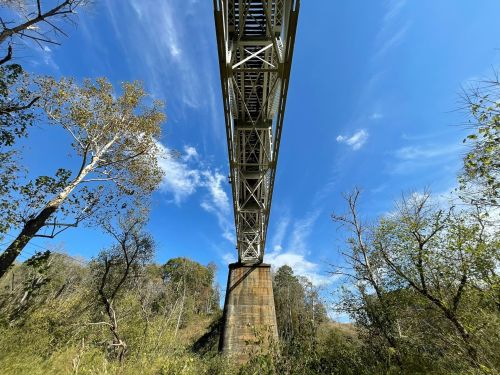 A metal bridge spans above a lush landscape, with trees and blue sky visible beneath it.
