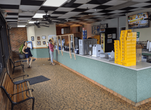 A bright, casual ice cream shop interior with a counter, benches, and customers ordering.
