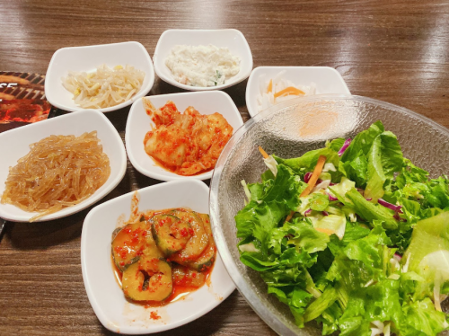 A variety of Korean side dishes in small bowls, including kimchi, pickled vegetables, and a fresh salad.