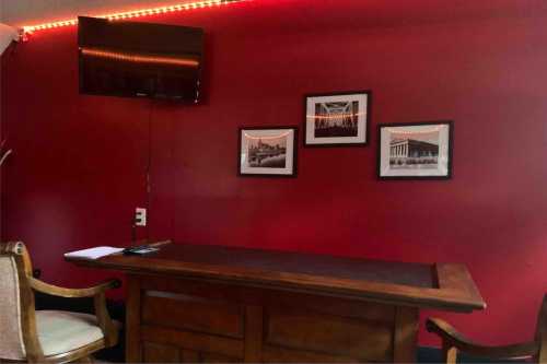 A wooden desk in a room with red walls, a TV, and three framed pictures hanging above.