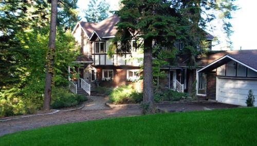 A large, two-story house surrounded by trees, with a winding path and a garage on the side. Lush green grass in the foreground.