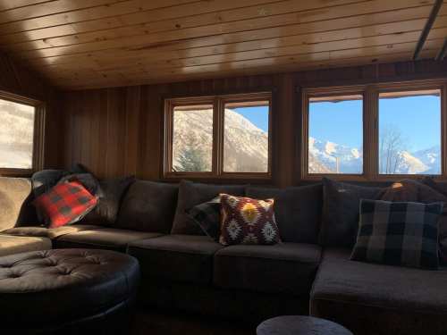 Cozy interior of a cabin with a sectional sofa and large windows showcasing a mountain view.