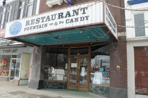 Historic restaurant entrance with a fountain and candy shop sign, featuring a wooden door and decorative awning.