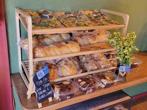 A wooden display rack filled with various baked goods, including pastries, bread, and brownies, with a small plant on top.