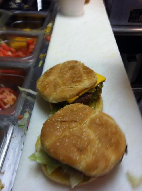 Two cheeseburgers with lettuce and cheese on a countertop, surrounded by fresh toppings in the background.