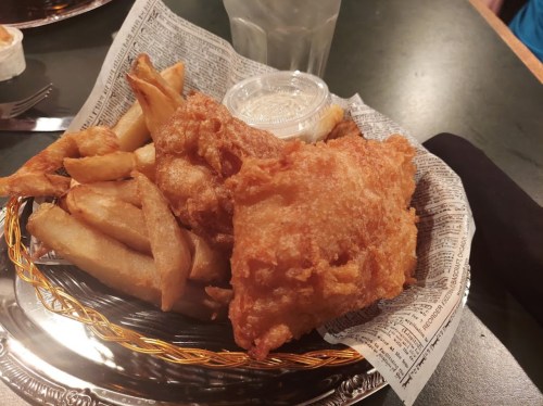 A plate of golden fried fish and crispy fries served with a small cup of dipping sauce.