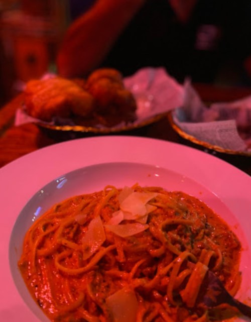 A plate of pasta in a creamy sauce with cheese, set against a dimly lit background with another dish in the distance.
