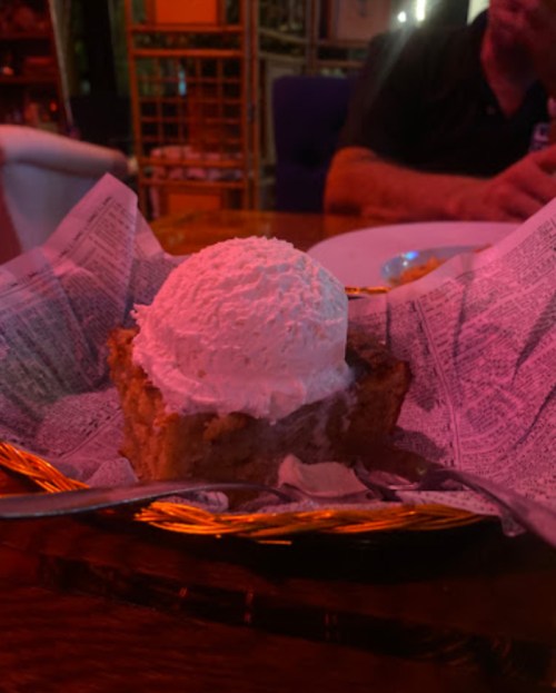 A slice of cake topped with a scoop of vanilla ice cream, served in a woven basket lined with newspaper.