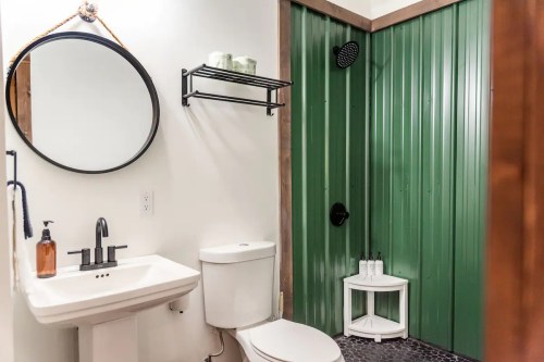 Modern bathroom featuring a round mirror, sink, toilet, and a green shower area with a black showerhead.
