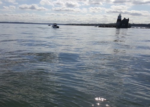 A calm water scene with a lighthouse in the distance and a small boat nearby under a partly cloudy sky.