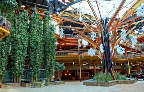 Interior of a spacious atrium featuring tall trees, modern architecture, and decorative elements hanging from the ceiling.