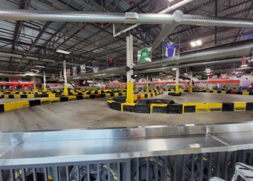 Indoor go-kart track with winding paths, black and yellow barriers, and a spacious, well-lit environment.