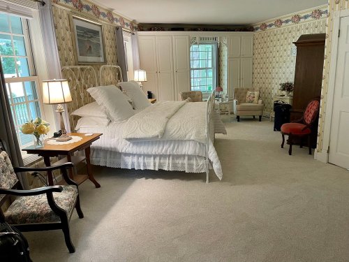 Cozy bedroom with a large bed, floral wallpaper, armchairs, and soft lighting from bedside lamps.